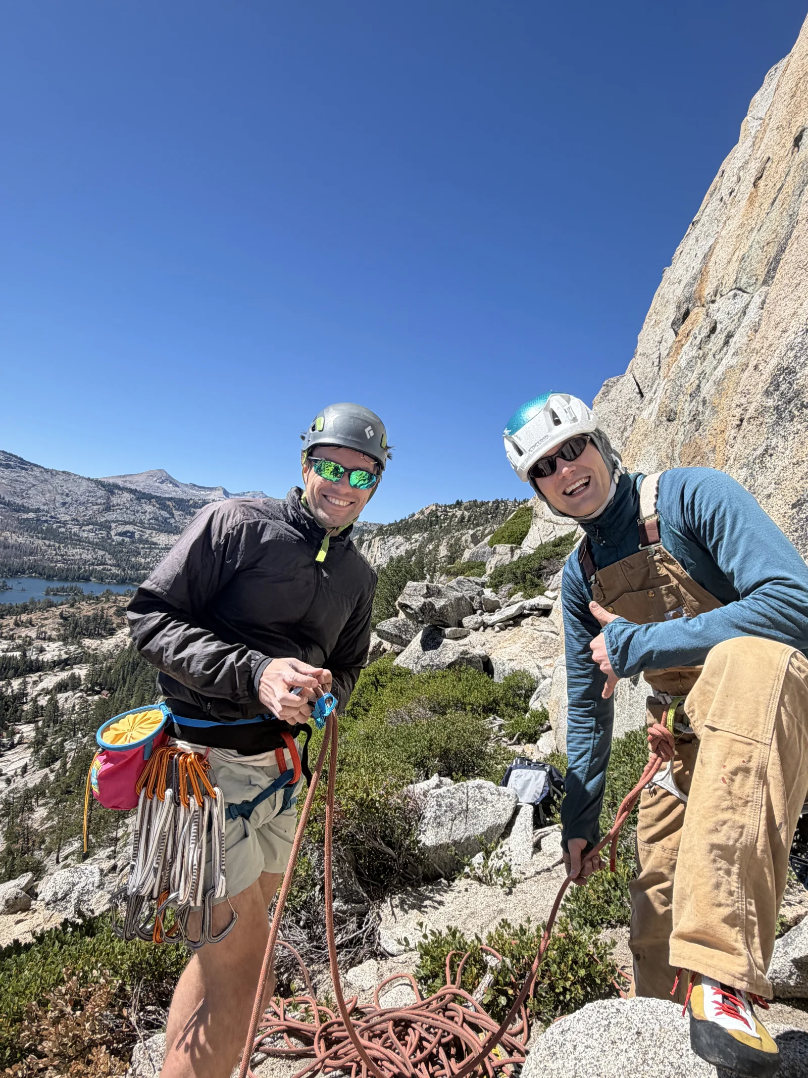 Two team members wearing climbing helmets beside a mountain rock face.